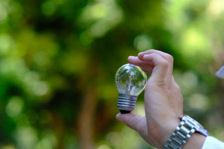 hand holding a light bulb with nature background. save energy concept.