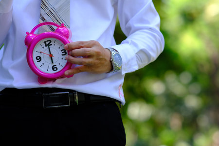 Businessman holding a pink alarm clock in his hands. Time management concept.