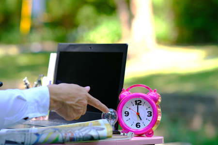 Businessman working in the park with a laptop and alarm clock.