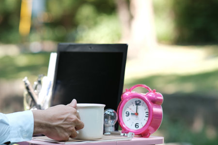Man holding a cup of coffee and a laptop in the park.