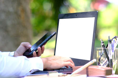 Businessman working with mobile phone and laptop on wooden desk in the garden