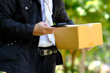 Delivery man with parcel and mobile phone in his hand, close up