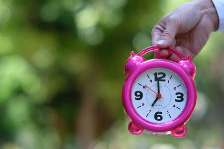 Pink alarm clock in hand on blurred green background. Time management concept.