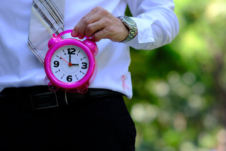 Businessman holding a pink alarm clock in his hand. Selective focus.