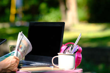 Close-up of a woman's hand holding a cup of coffee, a laptop and a newspaper.