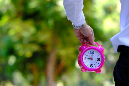 A man holds a pink alarm clock in his hand. Time management concept.