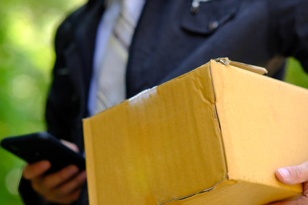 Close-up of a man holding a cardboard box and a smartphone