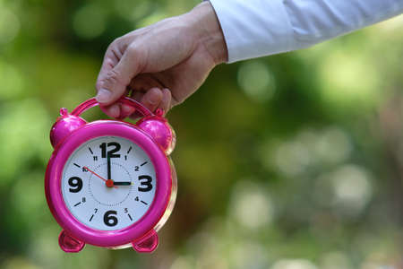 Hand holding pink alarm clock on blurred background, closeup. Time management