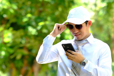 Handsome asian man in white shirt and cap using smartphone