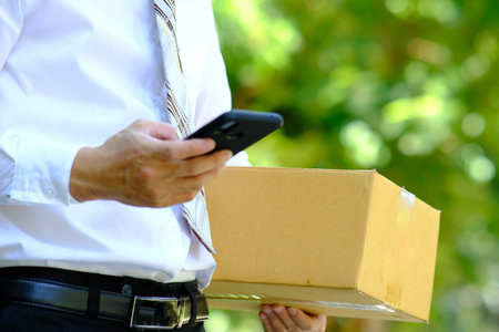 Businessman holding a cardboard box and using a smart phone for online shopping