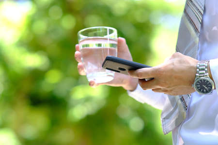 Man holding a glass of water and a smartphone in his hand.