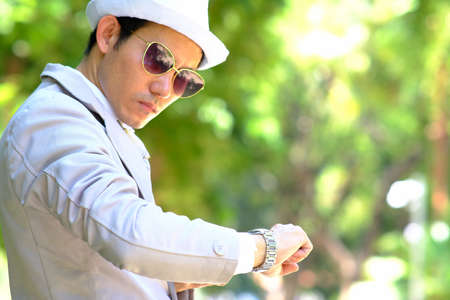 Young asian man wearing a white hat and sunglasses looking at his watch