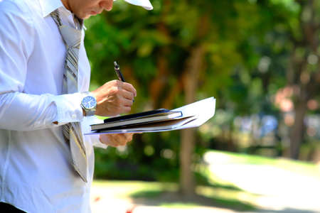 Businessman holding a pen and writing on a clipboard in the park