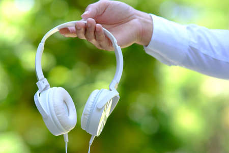White headphones in the hands of a man on a green background.