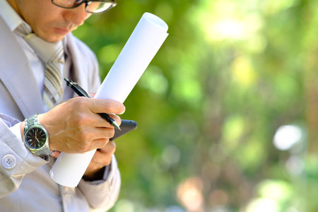 Businessman holding a pen and checking the blueprints in the parkの写真素材