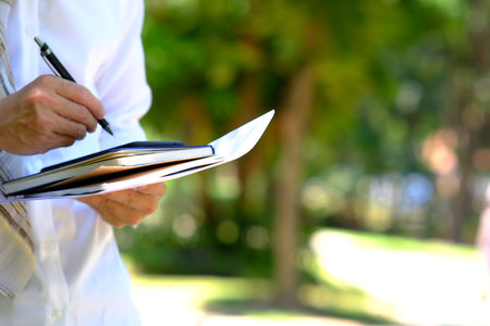 Businessman holding notebook and pen in park, closeup. Space for text