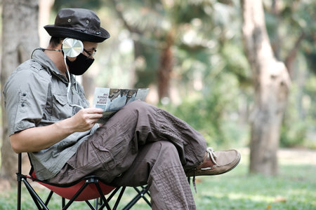 Asian man wearing face mask and reading newspaper while sitting in the park.の写真素材