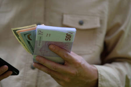 A man in a beige jacket holds a wallet with money in his hands.