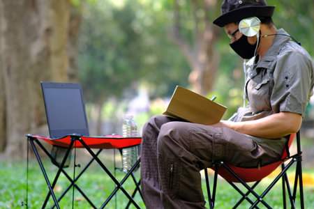 Young man wearing mask and using laptop in the park. Work from home concept.