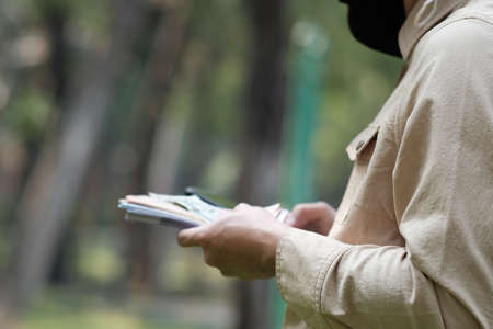 Close-up of a man in a protective mask counting money in the parkの写真素材