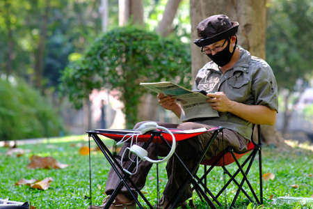 Young man wearing face mask reading newspaper in the public park. Coronavirus concept.の写真素材