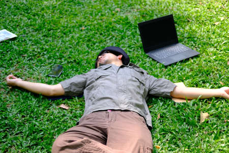 Young man lying on the grass with laptop and tablet in the parkの写真素材