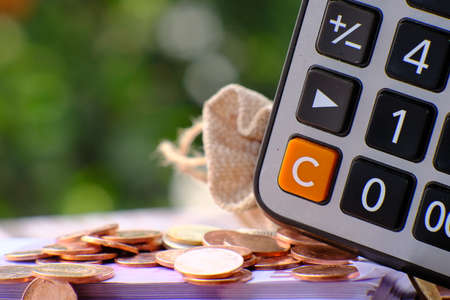 Calculator and coins on the table in the garden. Saving money concept.の写真素材