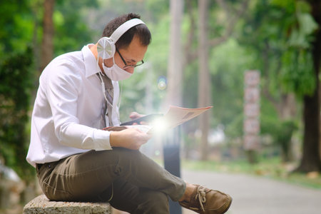 Young businessman wearing face mask and using tablet computer in the park.の写真素材