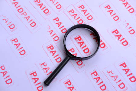 A magnifying glass on a paper with the word PAID.の写真素材