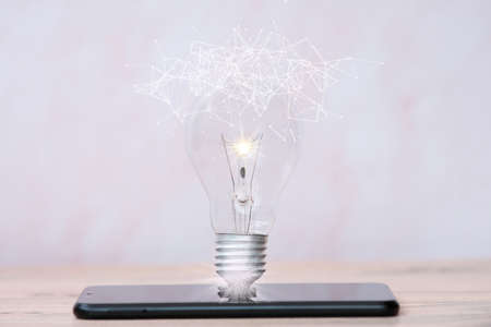 Smartphone with glowing light bulb on table, closeup. Idea conceptの写真素材