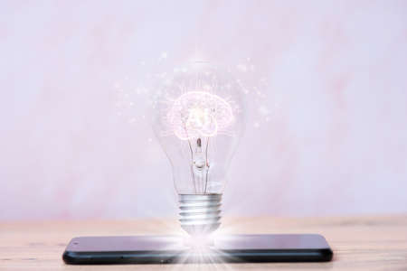Smartphone with glowing light bulb on table, closeup. Idea conceptの写真素材