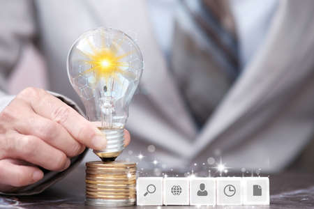 Businessman holding lightbulb on stack of coins, closeupの写真素材