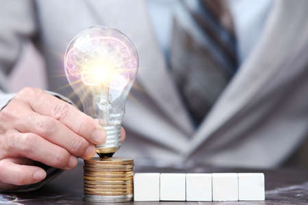 Businessman holding a light bulb on top of stack of coins. Idea and innovation conceptの写真素材