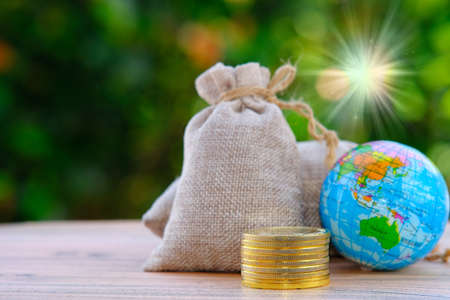 Globe and money bag on wooden table with green bokeh backgroundの写真素材