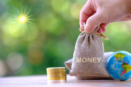 Hand putting money bag with money coins and word money on green bokeh backgroundの写真素材