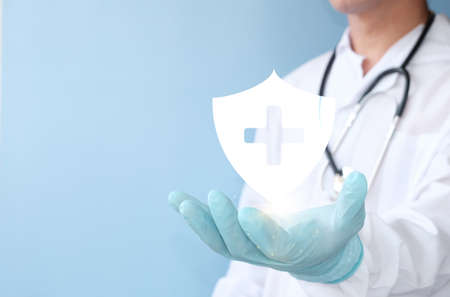 Doctor holding medical shield on blue background, closeup. Space for textの写真素材