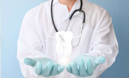 Doctor holding a stethoscope and a model of a tooth on a blue backgroundの写真素材