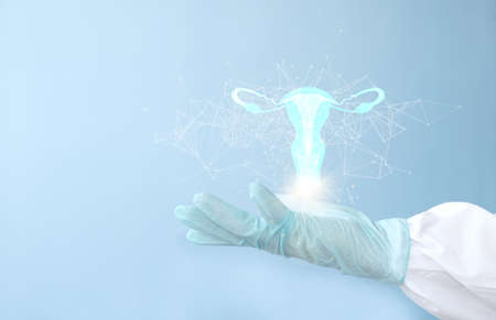 Female doctor hand in medical gloves holding digital hologram of uterus on light blue background, closeup. Gynecology conceptの写真素材