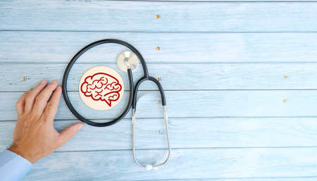 Doctor's hand holding a stethoscope with brain on a wooden background.の写真素材