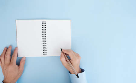 Top view of man writing in notebook on blue background with copy space