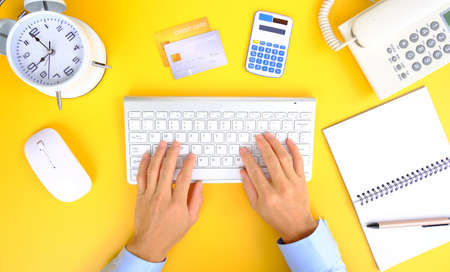 Top view of woman hands typing on laptop keyboard, credit card and alarm clock on yellow background