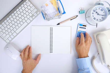 Top view of businessman working with calculator and laptop on white table, closeup