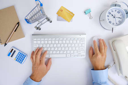 Top view of male hands typing on computer keyboard and shopping cart on white backgroundの写真素材