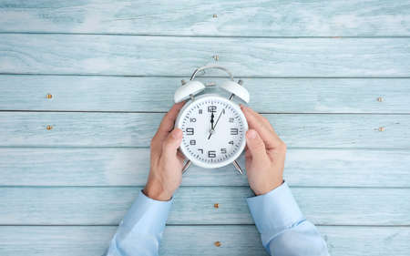 Man holding alarm clock on wooden background, top view. Time managementの写真素材