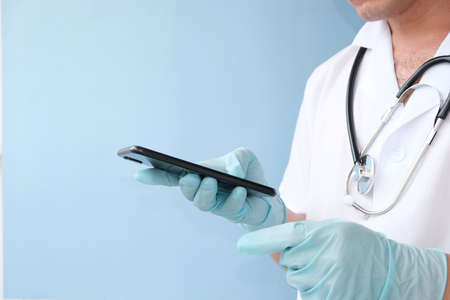 Doctor with stethoscope holding smartphone on blue background, closeup. Space for textの写真素材
