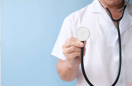 Doctor holding stethoscope on blue background, closeup. Space for text