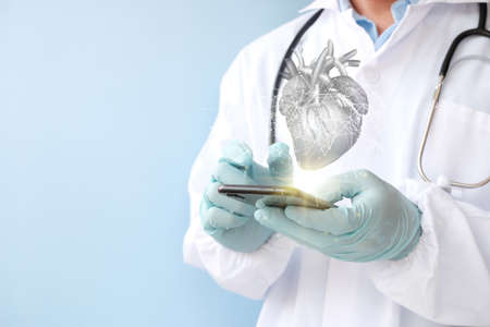 Doctor holding mobile phone with human heart on light blue background, closeup. Cardiology conceptの写真素材
