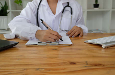 Close up of female doctor writing prescription or filling up medical form while sitting at the table.の写真素材