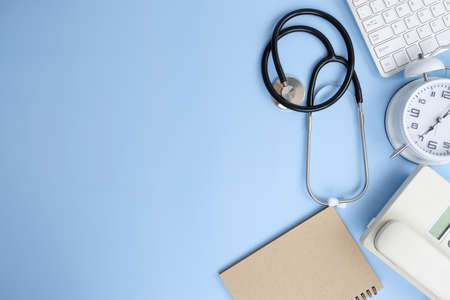 Flat lay composition with stethoscope and computer keyboard on light blue background. Space for text