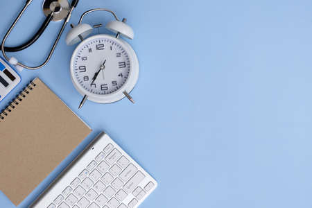 Flat lay composition with alarm clock, keyboard and notebook on light blue background. Space for textの写真素材